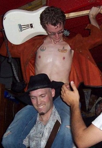 Tweed plays guitar behind his head while riding on another guitar player's shoulders
